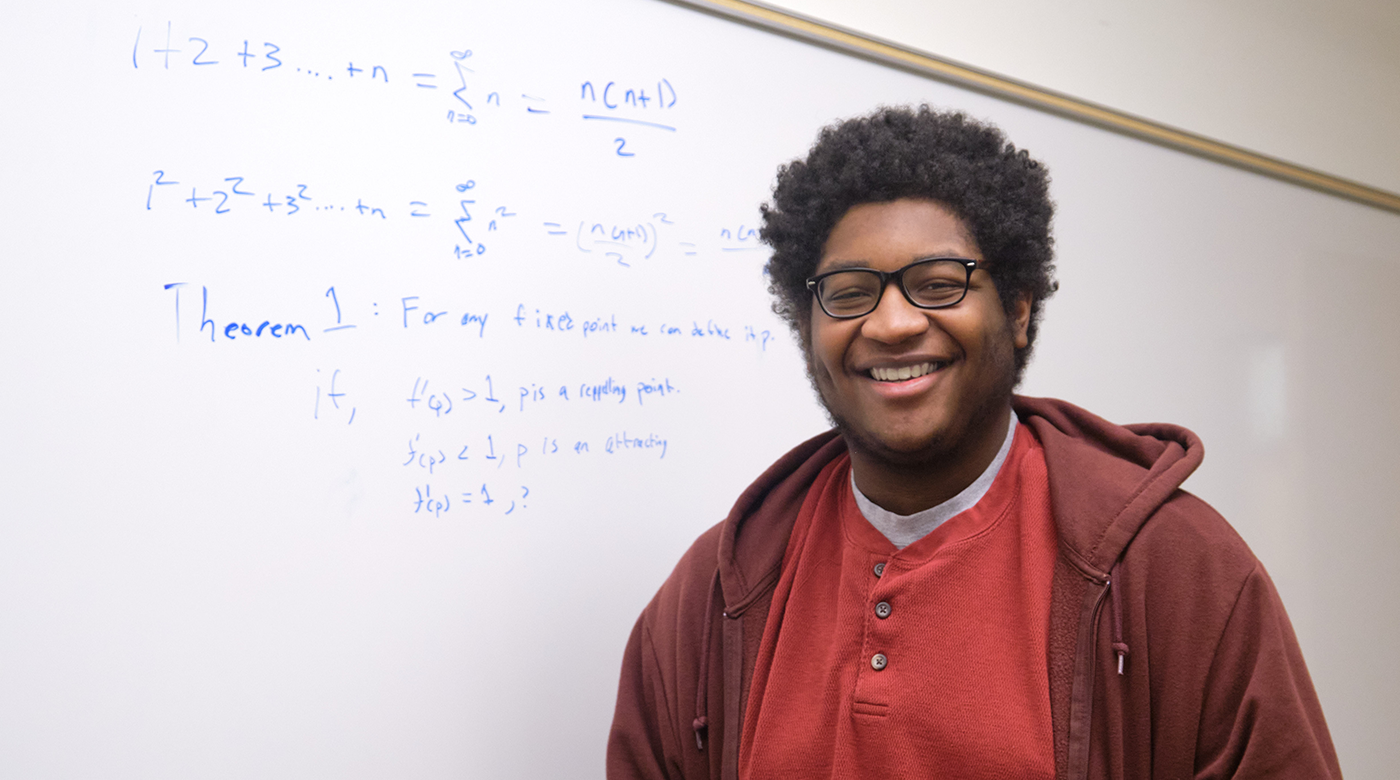 Image of Kevin-Canady-Pete standing in front of white board with math problems in blue ink/marker.