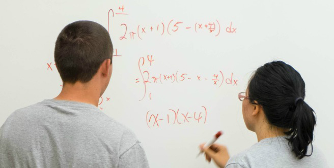 PLU math students working on a math problem on a white board. Students are faced towards the white board.
