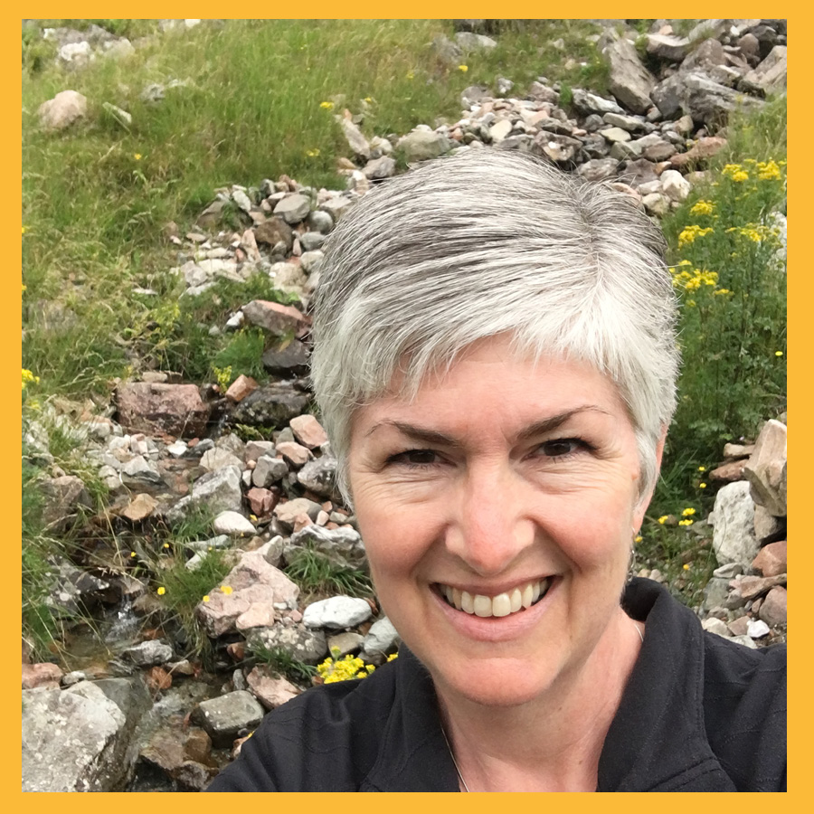 A smiling Ardys takes a selfie on a hiking trip with rocks and grass in the background.