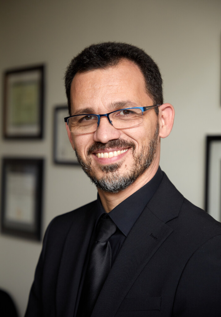 A formal headshot of Cassio, he's smiling and wearing a black suit and tie.