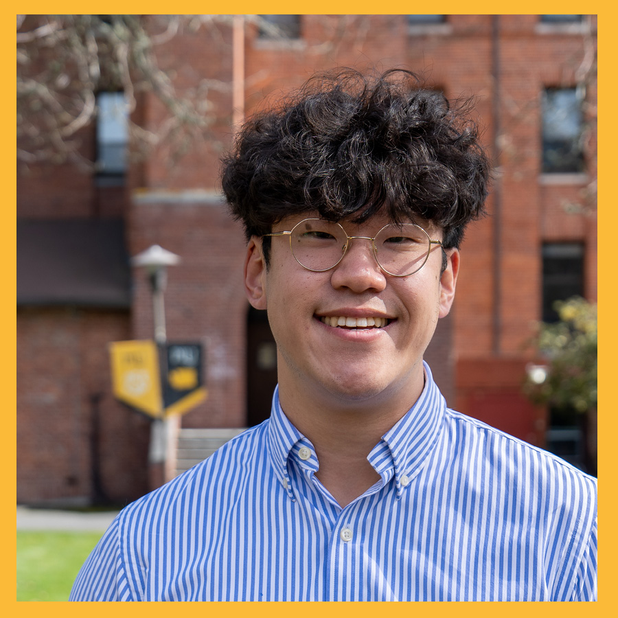 A smiling David is looking at the camera with Harstad Hall in the background