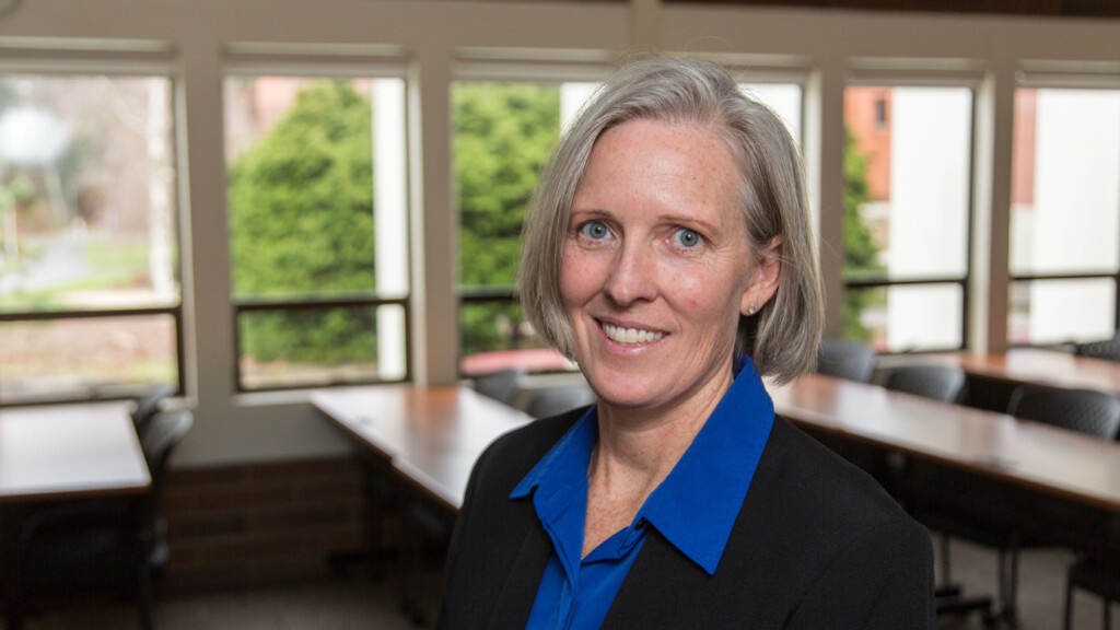 Karen McConnell smiling while standing in an empty PLU classroom.