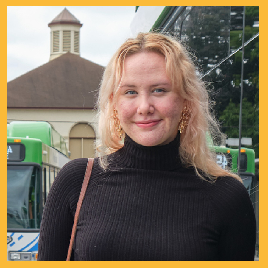 Kenzie posing for a portrait with a public transit stop in the background