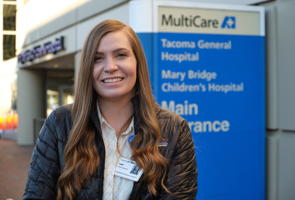 Leah Butters standing outside of Tacoma General Hospital with a blue "MultiCare" sign and logo above her left shoulder.