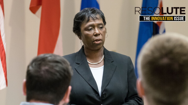 Michelle Y. Long,’85 presenting with flags behind her. she's wearing a black business suit