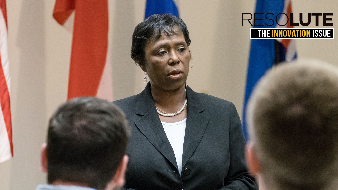 Michelle Y. Long,’85 presenting with flags behind her. she's wearing a black business suit