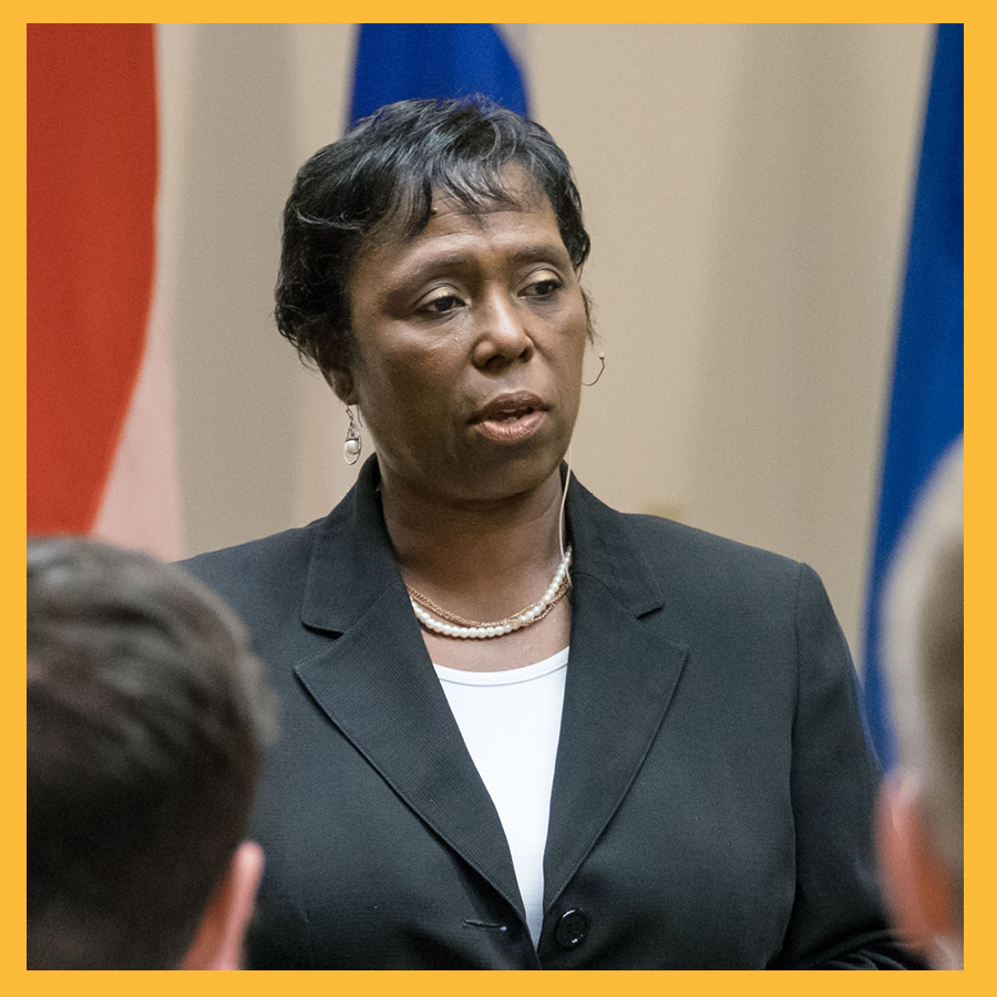 Michelle Y. Long,’85 presenting with flags behind her. she's wearing a black business suit