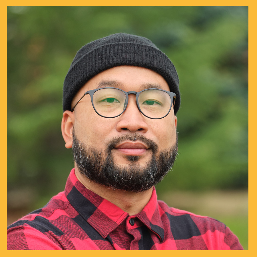 A headshot of Silong Chunn, he's wearing a black beannie hat, black rimmed classes and a flanner shirt.