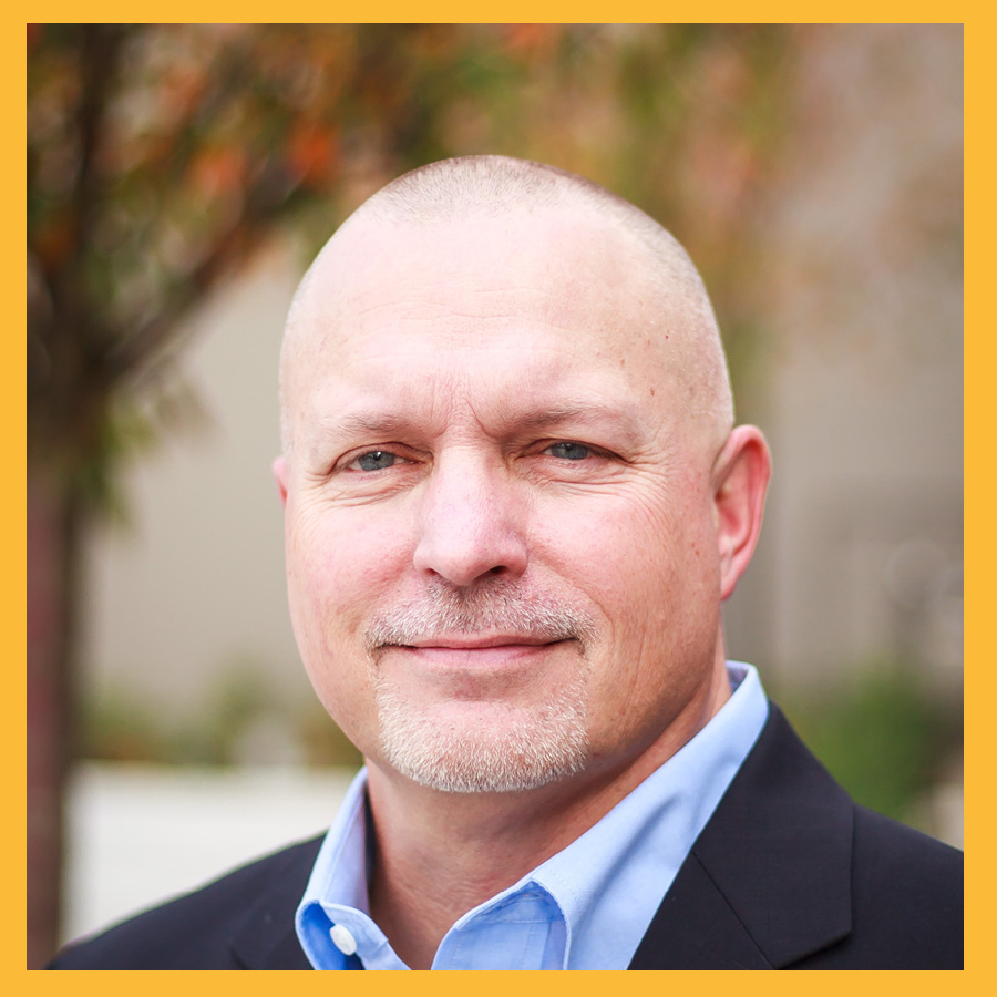 a professional business headshot of PLU regent Tom Saathoff ’87. He's wearing a black blazer over a light blue dress shirt and half smiling.