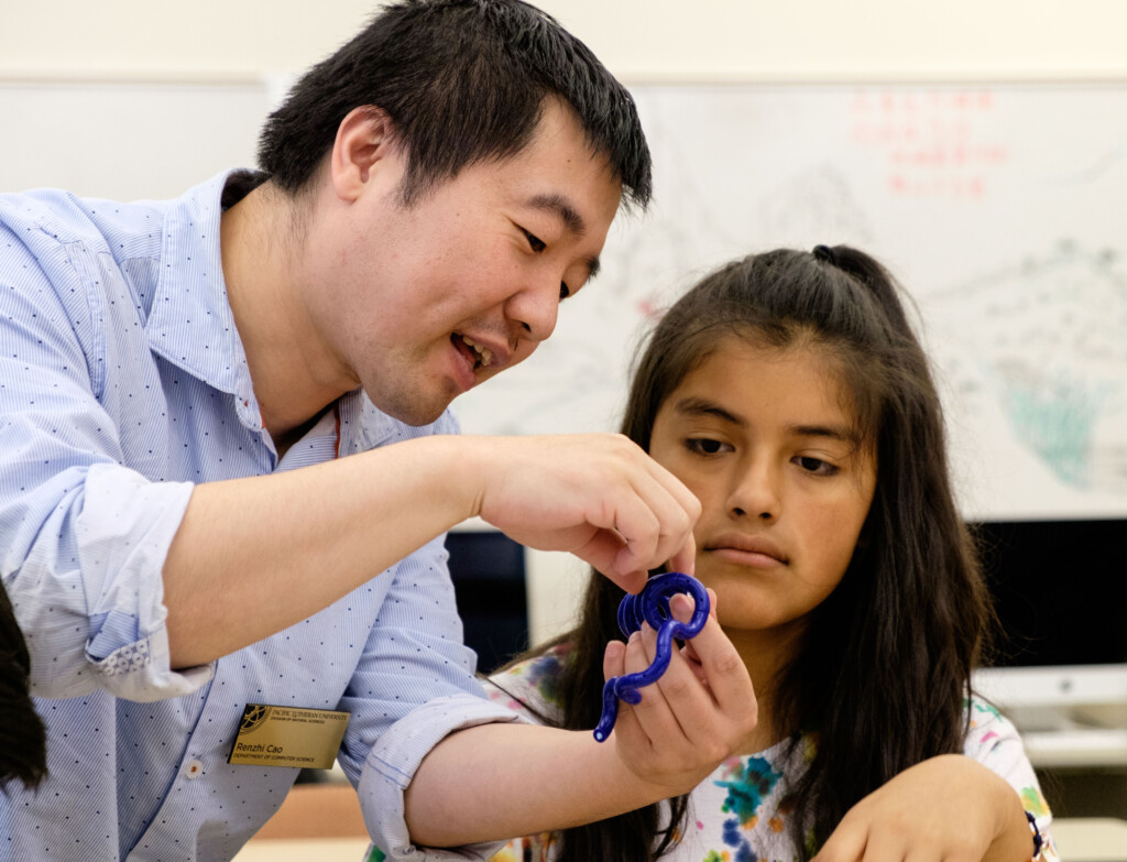 Professor Renzhi Cao holds a modeling tool while giving one on one instruction to a student