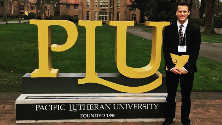 Parker Simpson stands to the side of PLU signage on Campus on Park Avenue
