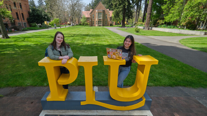 PLU monument sign with Jenny Kamimura and Isabella Daltoso with Xavier hall behind