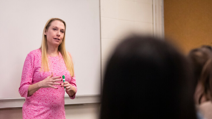 Beth Griech-Polelle wearing a pink dress giving a lecture in front of a classroom