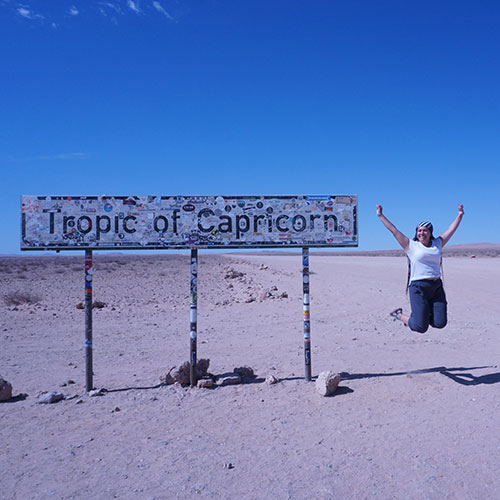 Elizabeth Larios jumping off the ground by the "Tropic of Capricorn" sign in Namibia, Africa
