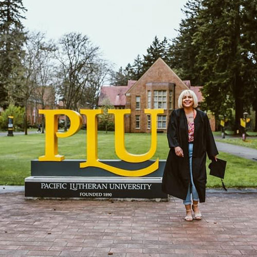 Elizabeth Larios standing in front of the PLU sign on campus after graduating