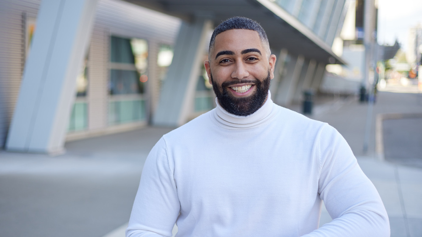Mycal Ford ’12 smiles into the camera. He's standing outside the Tacoma convention center and wearing a white turtle-neck sweater.