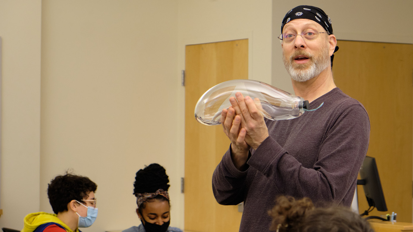Professor of Mathematics Daniel Heath holds up a glass biodome in the middle of a classroom