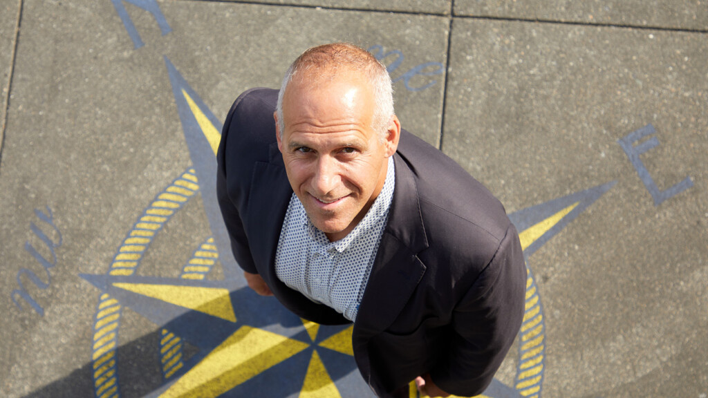 John Wolfe stands on a maritime star printed on a sidewalk at the Port of Tacoma. He's looking directly up at the photographer above him.