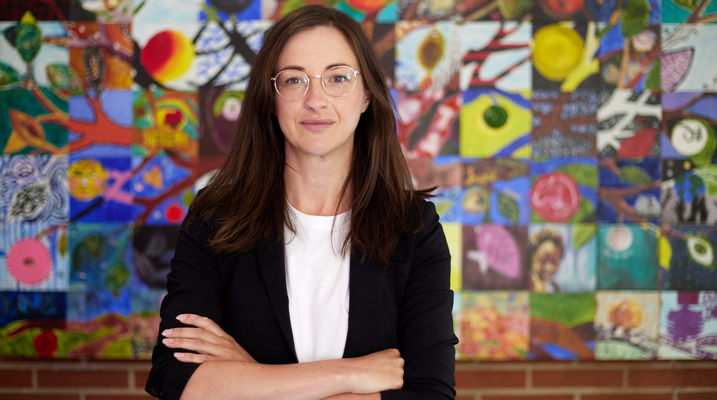 Marnie Ritchie poses with arms crossed in front of an artwork resembling a collage in the back ground.