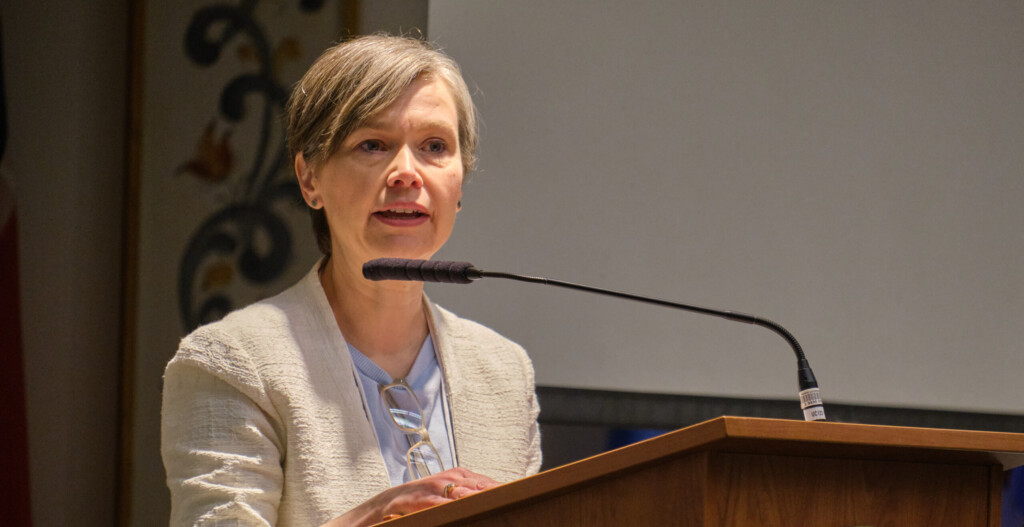 Sergia Hay wearing a blazer speakng from a podium with a PLU logo on it