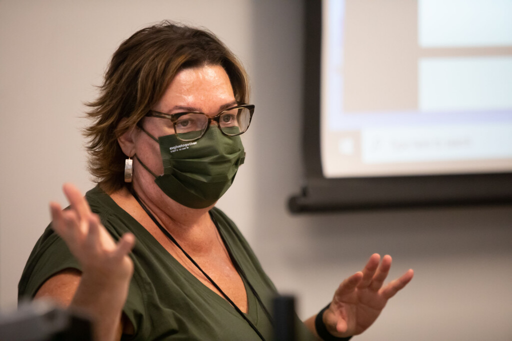 Professor Lisa Marcus, wearing an olive green protective mask and shirt, giving instructions at the front of the class.