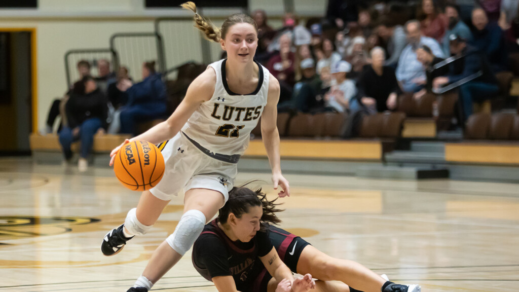 Sydney Reisner dribbles past a defender on the basketball court. Sydney is avoiding as the defender is falling to the ground.