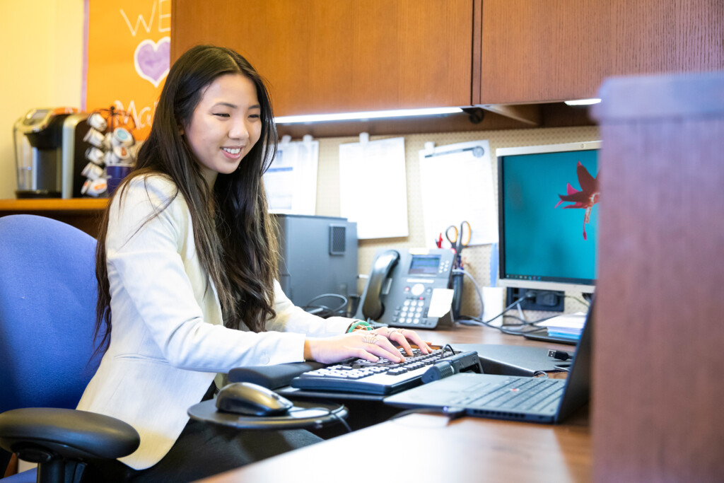 Quan Huynh ’25 sits at computer desk, typing on the keyboard - working in an office setting.