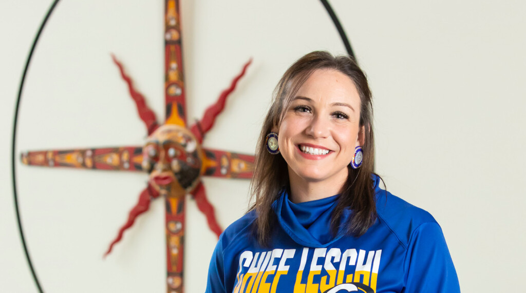 Leavens-featured Leavens smiles into the camera. she is wearing a bright blue sweatshirt that says 'CHIEF LESCHI' in white and gold letters.