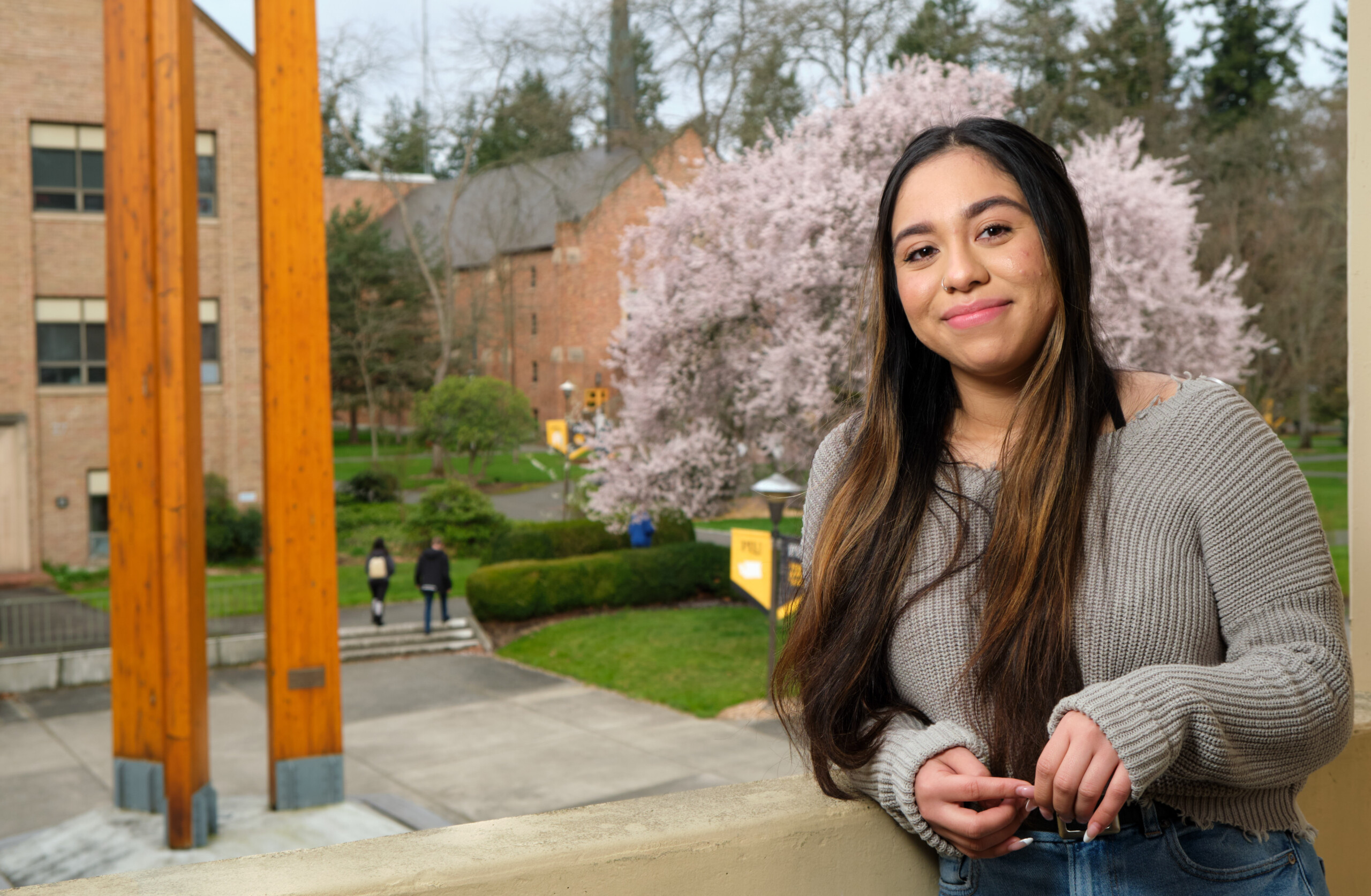 Social work alumna sarah saavedra poses for a photo on PLU's upper campus. She is smiling and wearing a grey sweater.