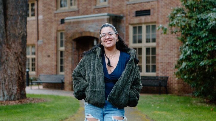 Stephanie Aparicio Zambrano walks down a path on PLU's upper campus. She is smiling and wearing a fleece jacket.