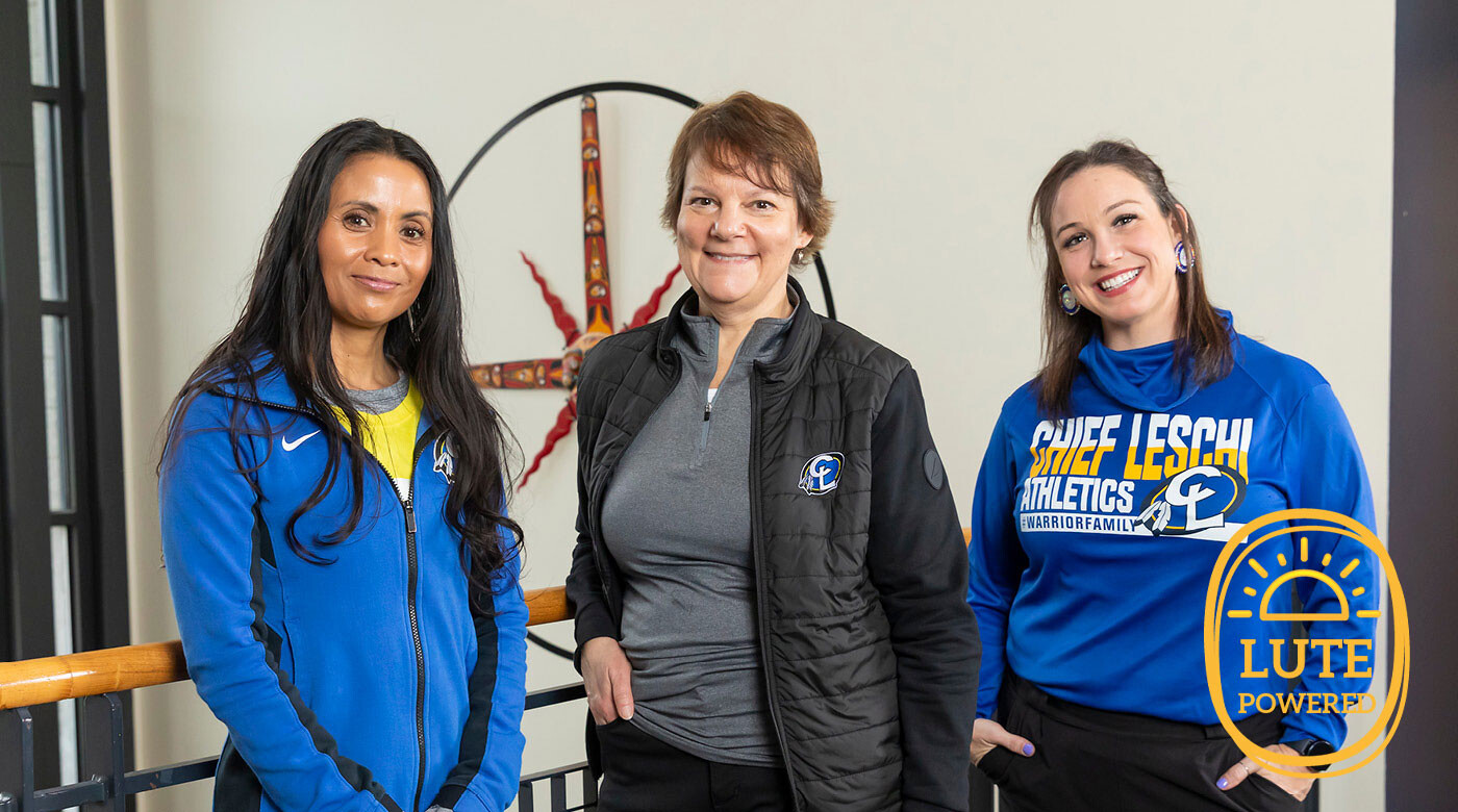 (From Left) Melanie Helle, Nancy Nelson, and Jenifer Leavens stand shoulder to shoulder in the lobby of Chief Leschi. They are all smiling and wearing Chief Leschi gear.