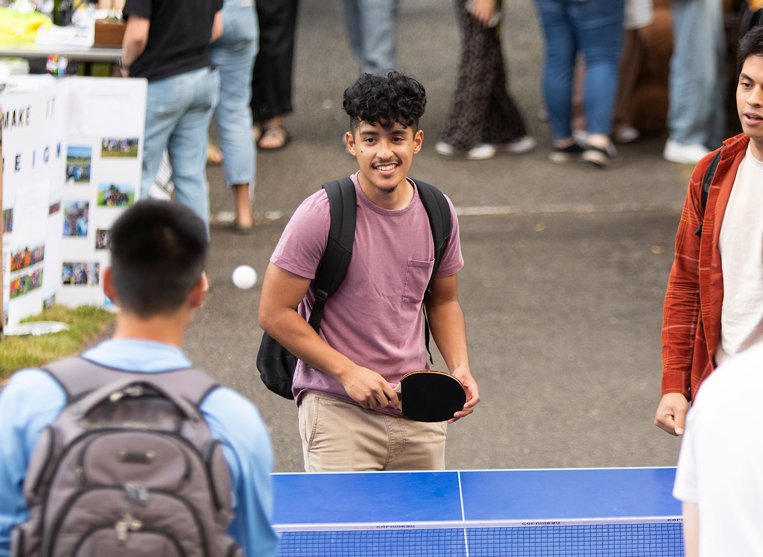 PLU students play ping pong at an outdoor involvement fair where all the student clubs have tables and talk to new students.