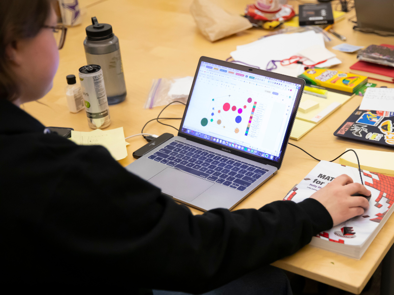 A student works on a lap top. The lap top is facing the camera and you can see the student is working on a math modeling problem on the screen.