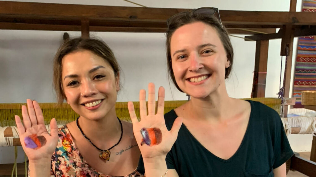 Surla and a fellow student hold up their hands to show dye stuck on their palms. They are both smiling and wearing t-shirts.