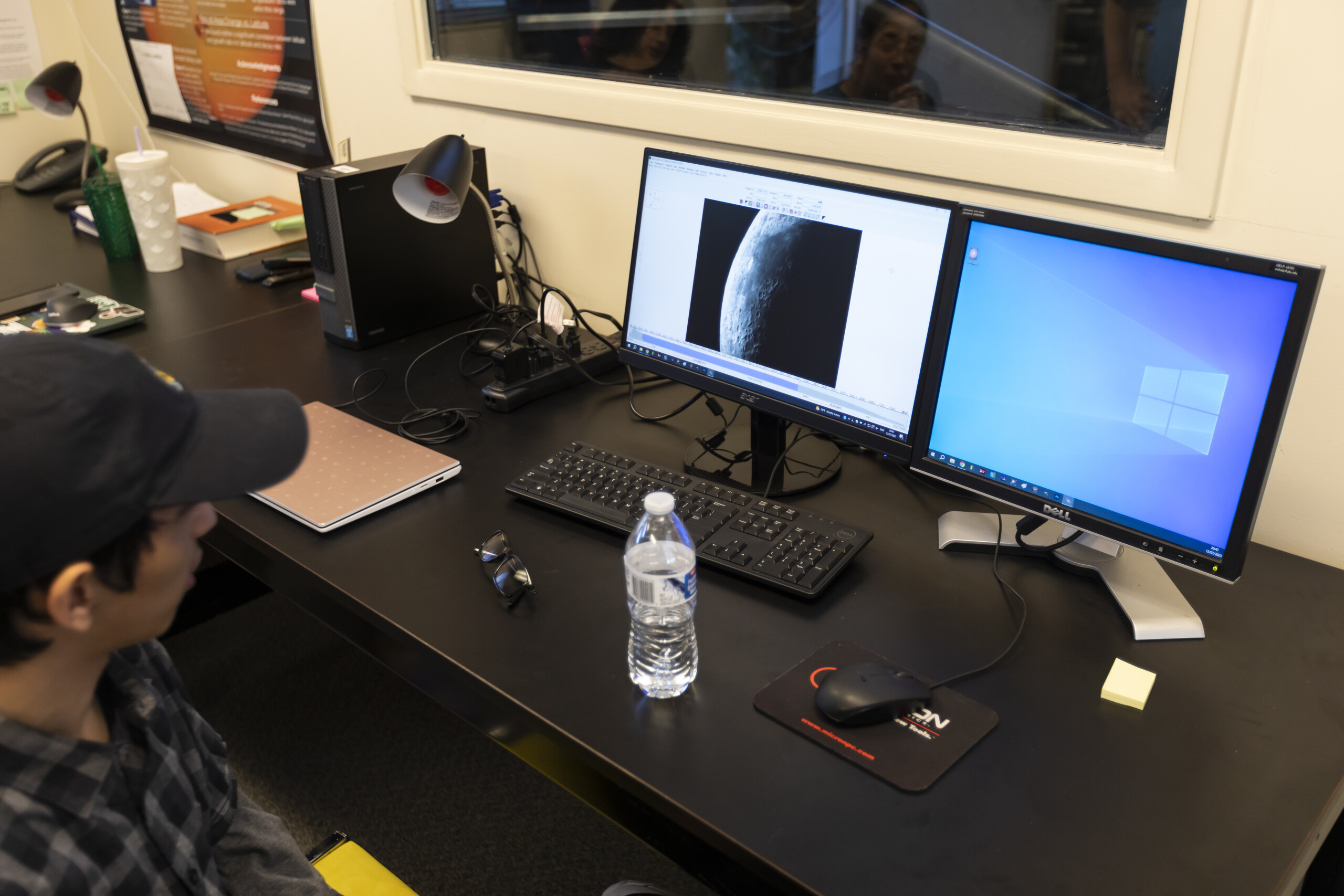 PLU student is sitting in front of two computer screens looking at the moon.