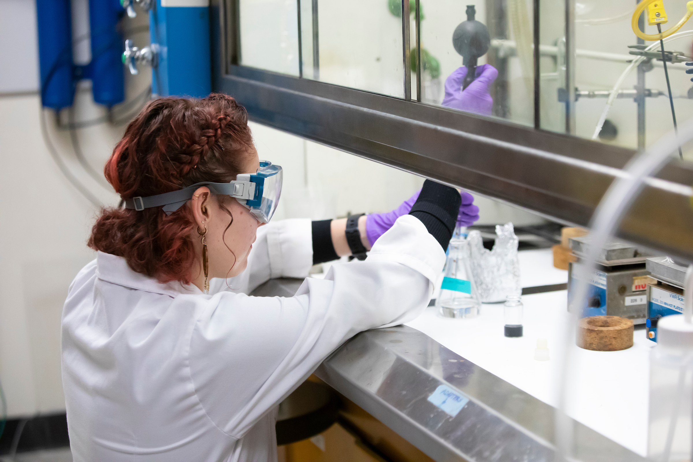 A PLU student is kneeling on the ground and piping liquid into a test tube in the chem lab.