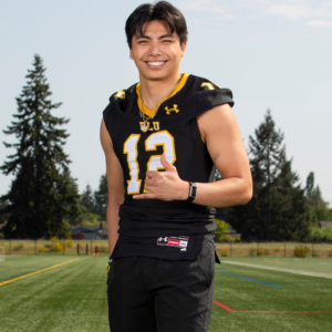 Football players stand on the practice field and smiles into the camera.