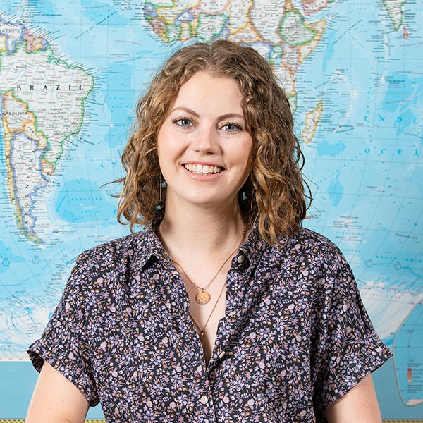 Ellie Dieringer sitting at a desk in a PLU clasroom with a big map of the world behind her.