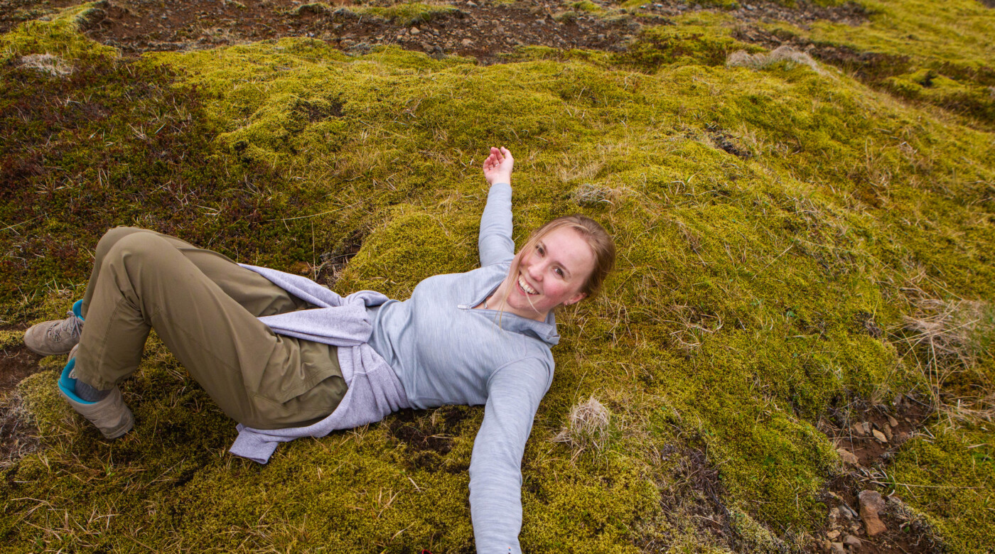 Student is lying on the grass on a mountain in Iceland and smiles into the camera.