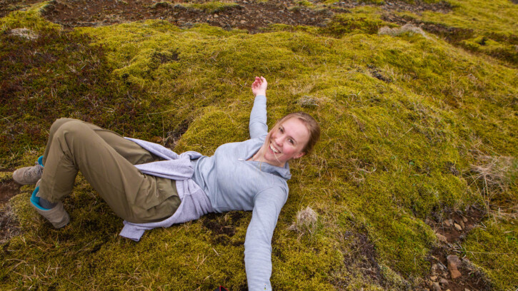 Student is lying on the grass on a mountain in Iceland and smiles into the camera.