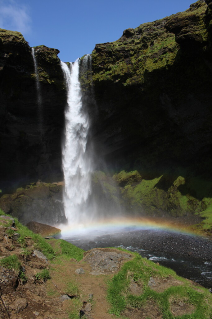 A photo of a waterfall with a rainbow where the falling water hits the water.