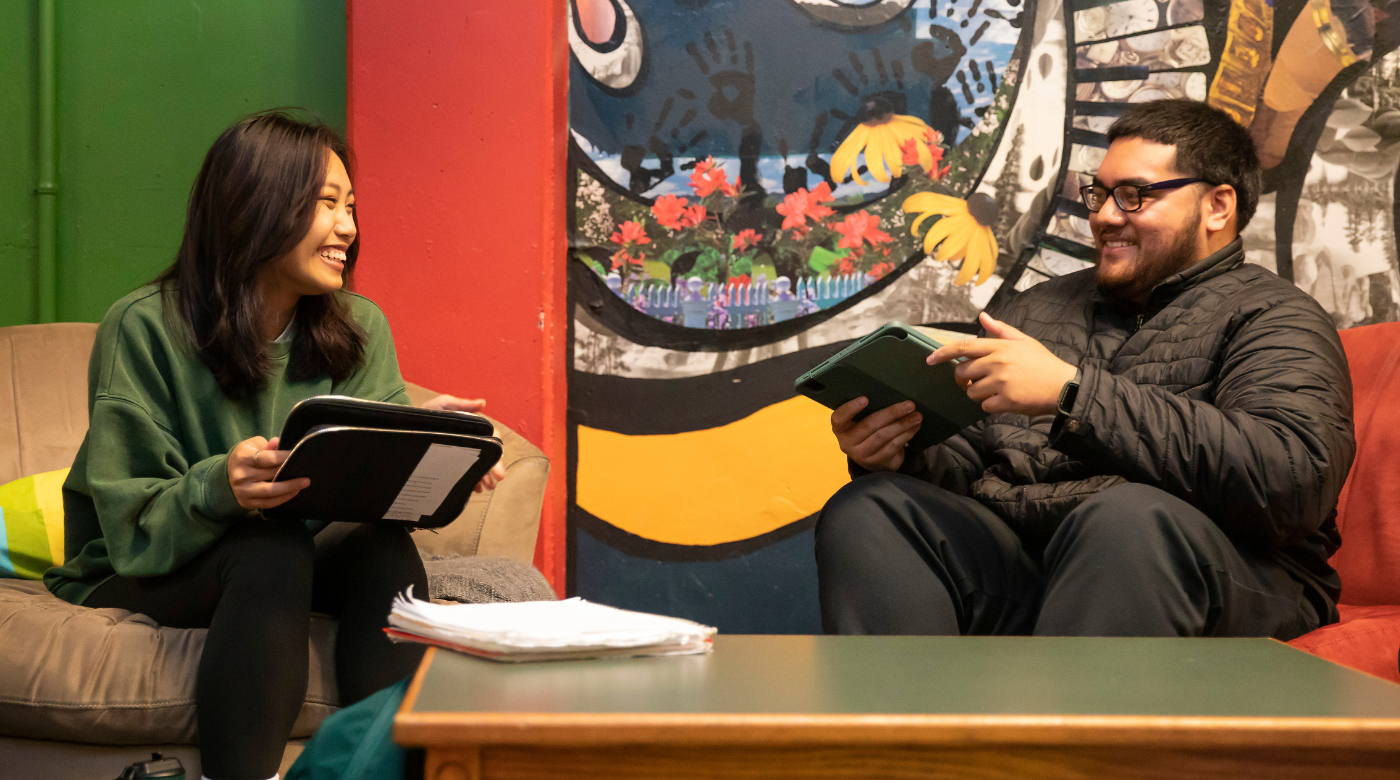 Two students talk to each other holding ipads.