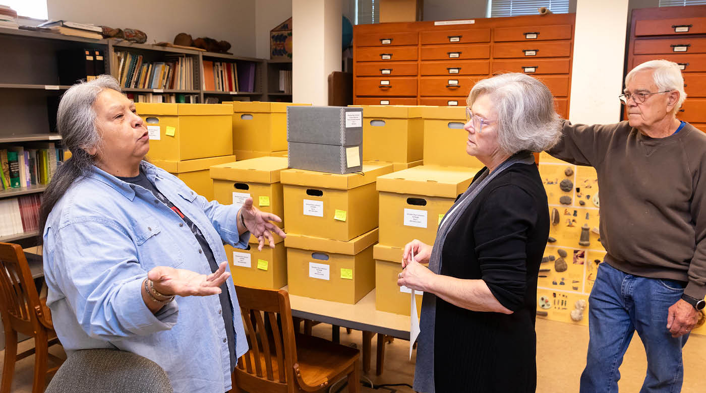 Annette Bullchild (Nettsie), the Nisqually Tribe’s historic preservation officer, speaks with PLU professors in Xavier Hall. Behind them are piles of boxes from the Woodard Bay collection.