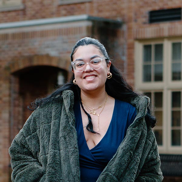 Stephanie Aparicio Zambrano walks down a path on PLU's upper campus. She is smiling and wearing a fleece jacket.