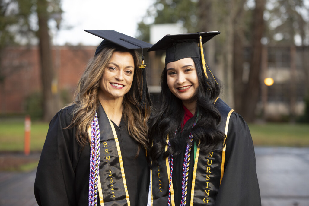 Millett (left) and Lopez (right) both decked out in PLU commencement robes on the day of their nursing pinning ceremony. They are smiling and standing in PLU's Red Square.