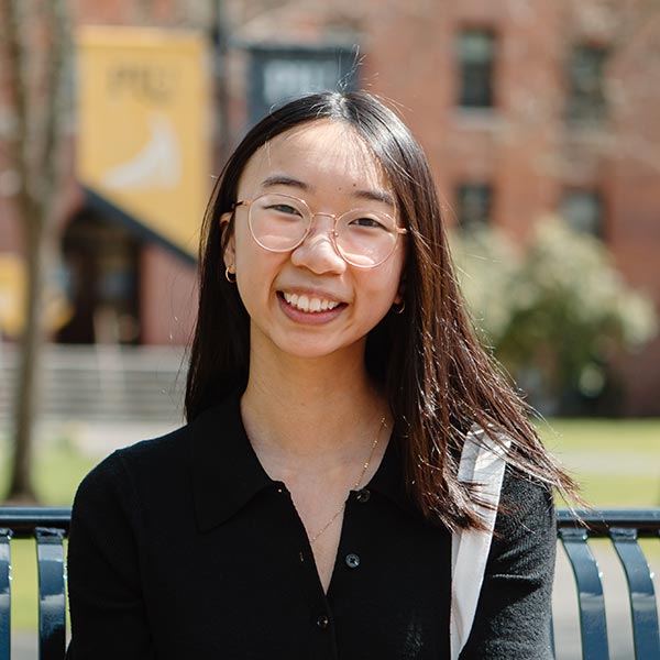 Tiffany Wong smiles into the camera with a brick campus building behind her.