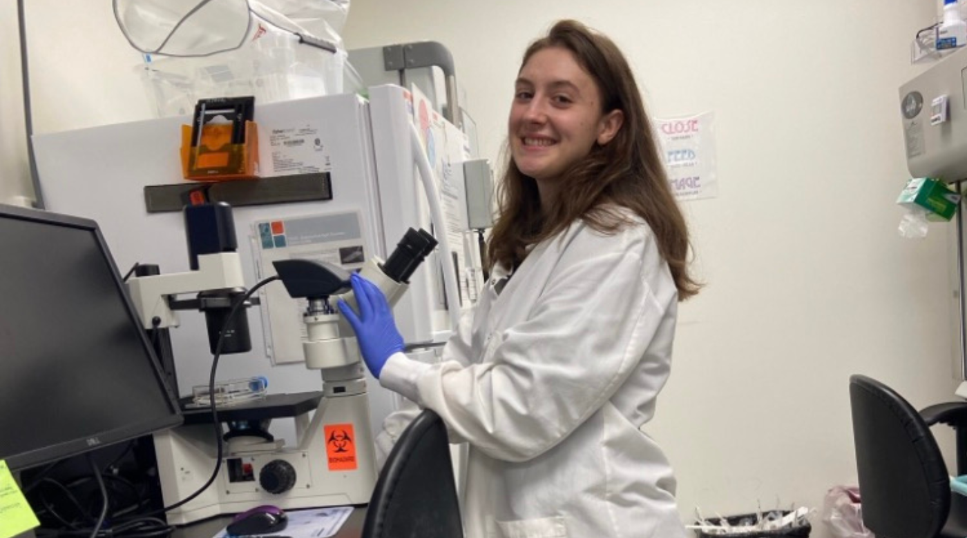 PLU student smiling at the camera next to a microscope