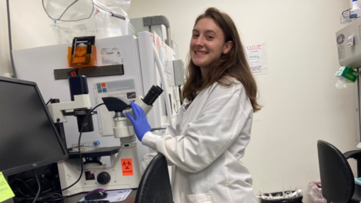 PLU student smiling at the camera next to a microscope