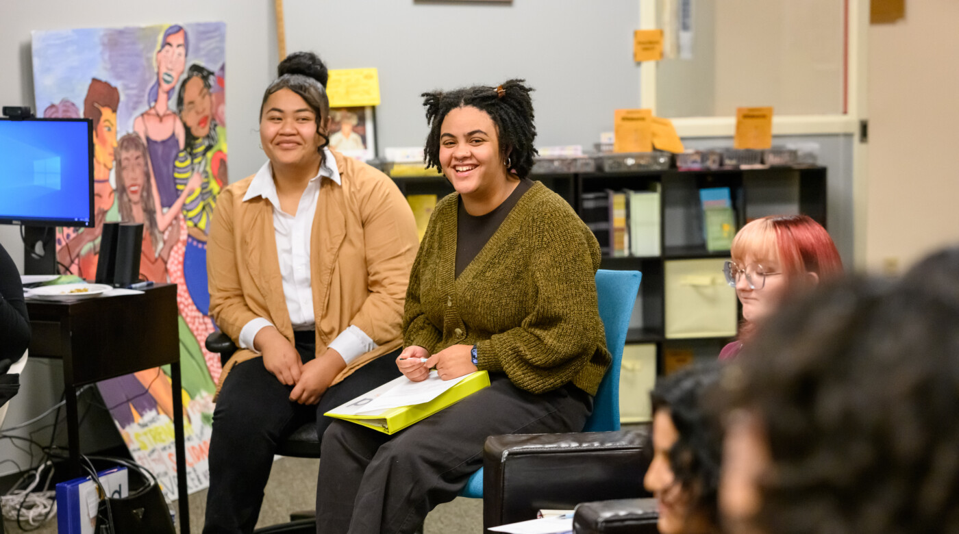 Two PLU students sit in a classroom and look into the camera.