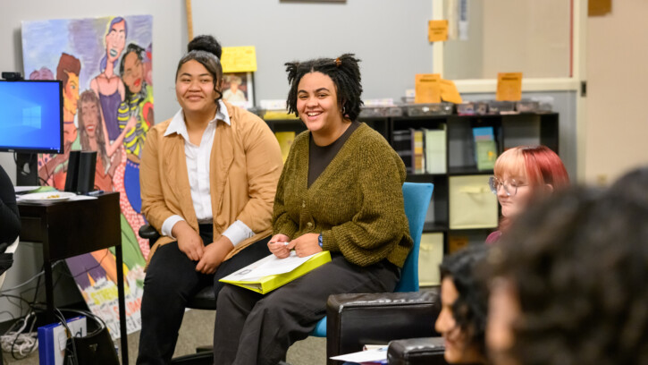 Two PLU students sit in a classroom and look into the camera.